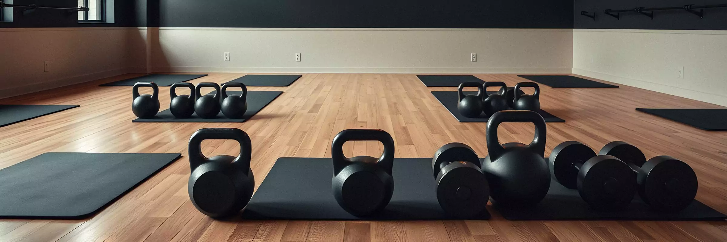 An empty studio set for class: mats, kettlebells and warm pendant lights